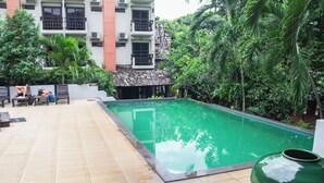 A swimming pool with tiled flooring, surrounded by greenery and a building with multiple balconies. - Sunday Rainforest Chiangmai Hotel  (Chiang Mai)