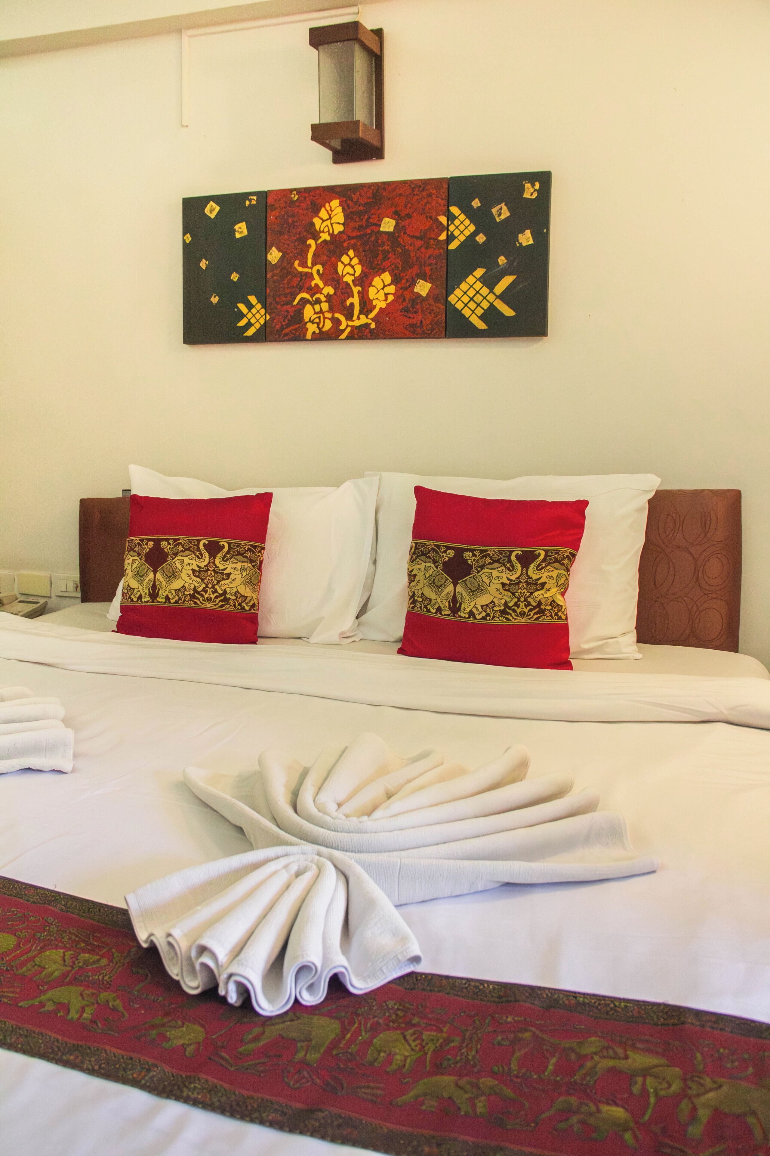 A hotel room with a neatly made bed, a decorative wall hanging, and a red patterned rug.