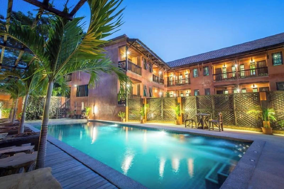 A hotel with a swimming pool, outdoor seating, and a multi-story building with balconies.
