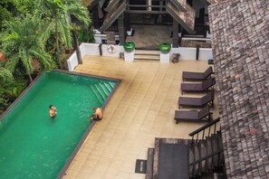 An outdoor swimming pool with two people, surrounded by lounge chairs and a tiled deck. - Sunday Rainforest Chiangmai Hotel  (Chiang Mai)