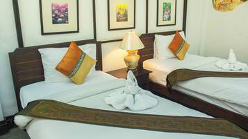 A hotel room with two beds, each with a pillow and a towel. There is a nightstand with a lamp between the beds. The walls have framed pictures.