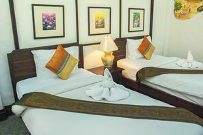 Habitación de hotel con dos camas, cada una con una almohada y una toalla.  Hay una mesita de noche con una lámpara entre las camas. Las paredes tienen cuadros enmarcados.