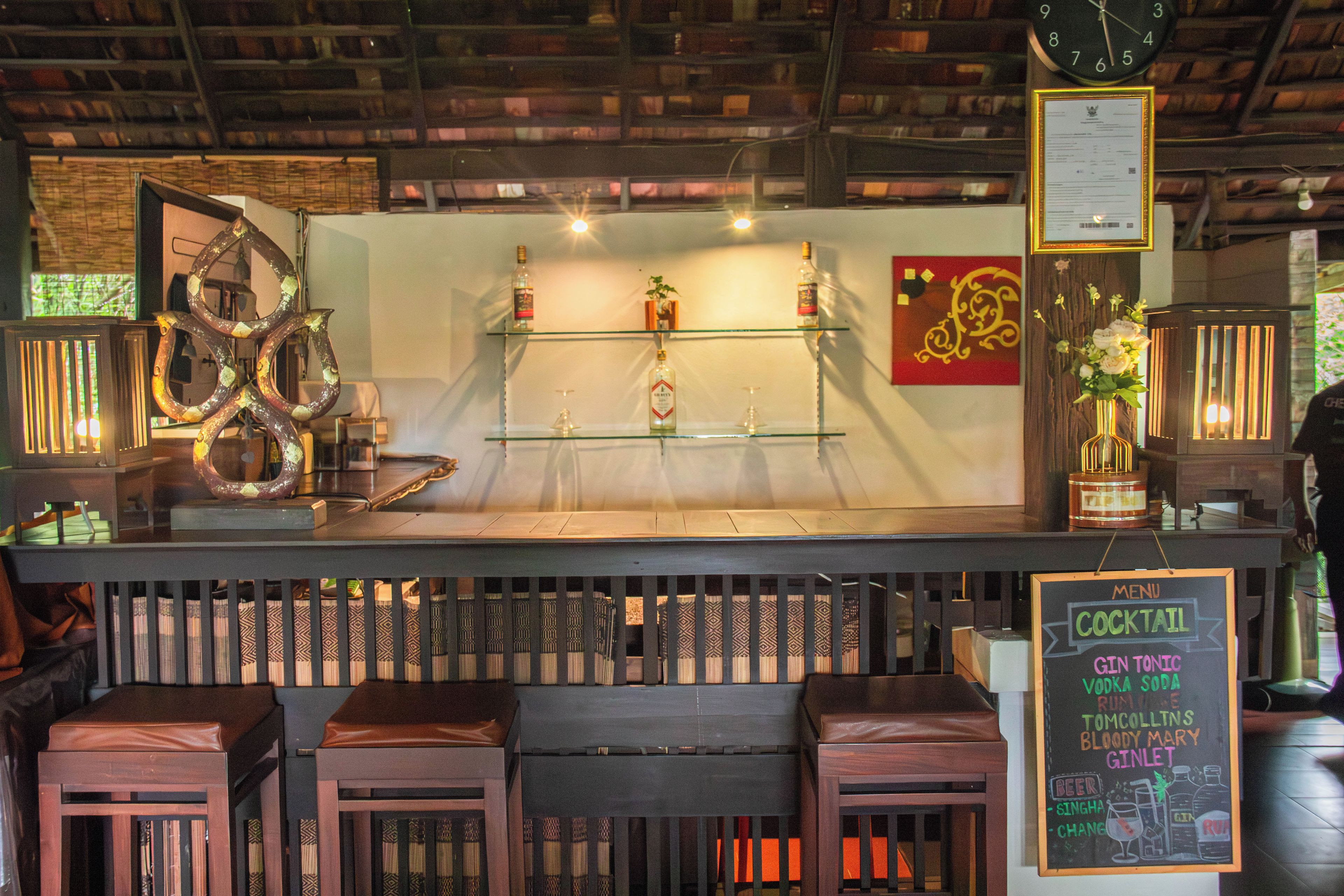 A bar area with shelves of bottles, a clock, and a chalkboard menu.