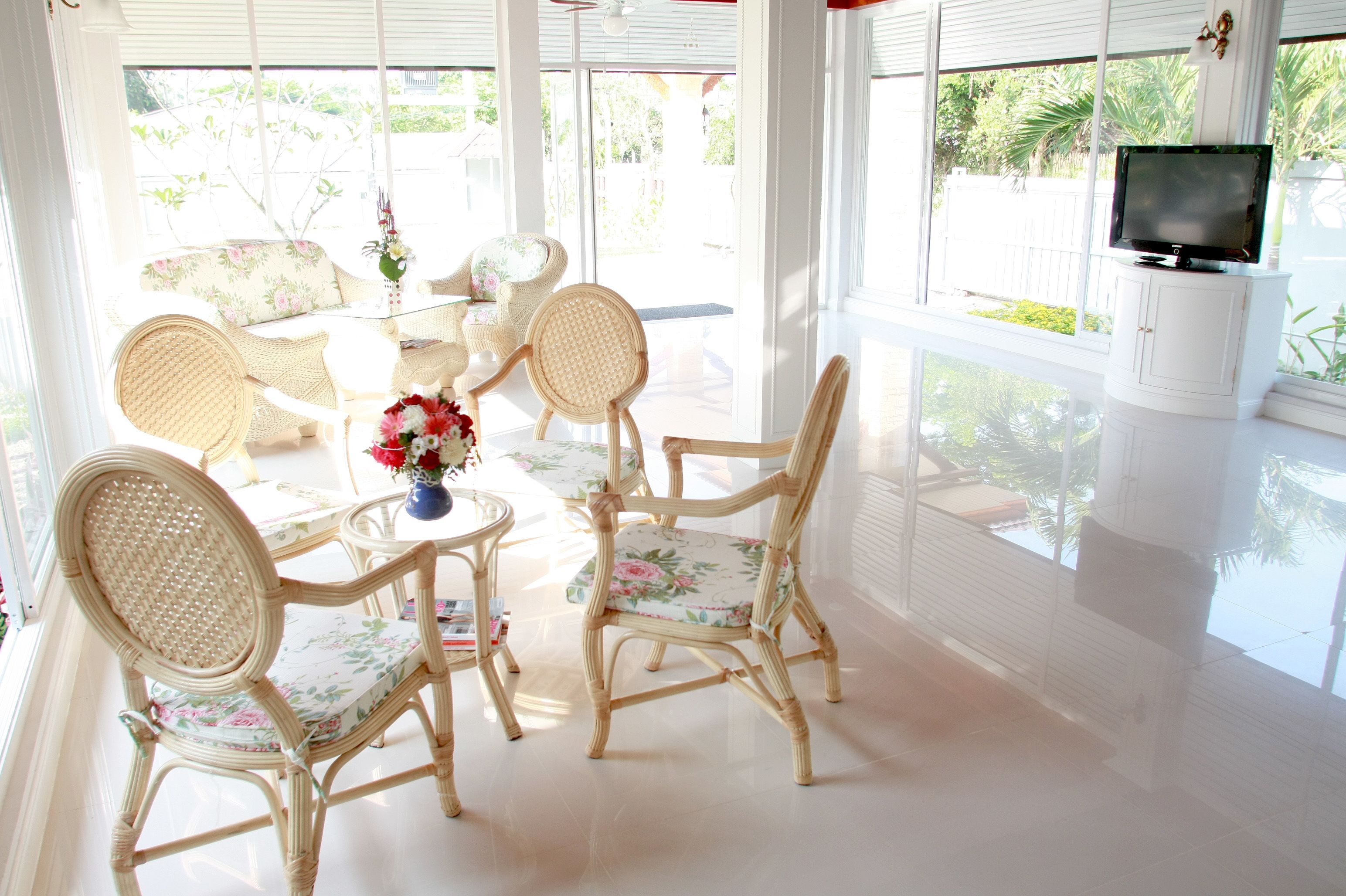 A bright, sunlit room with wicker furniture, a television, and a view of greenery outside.