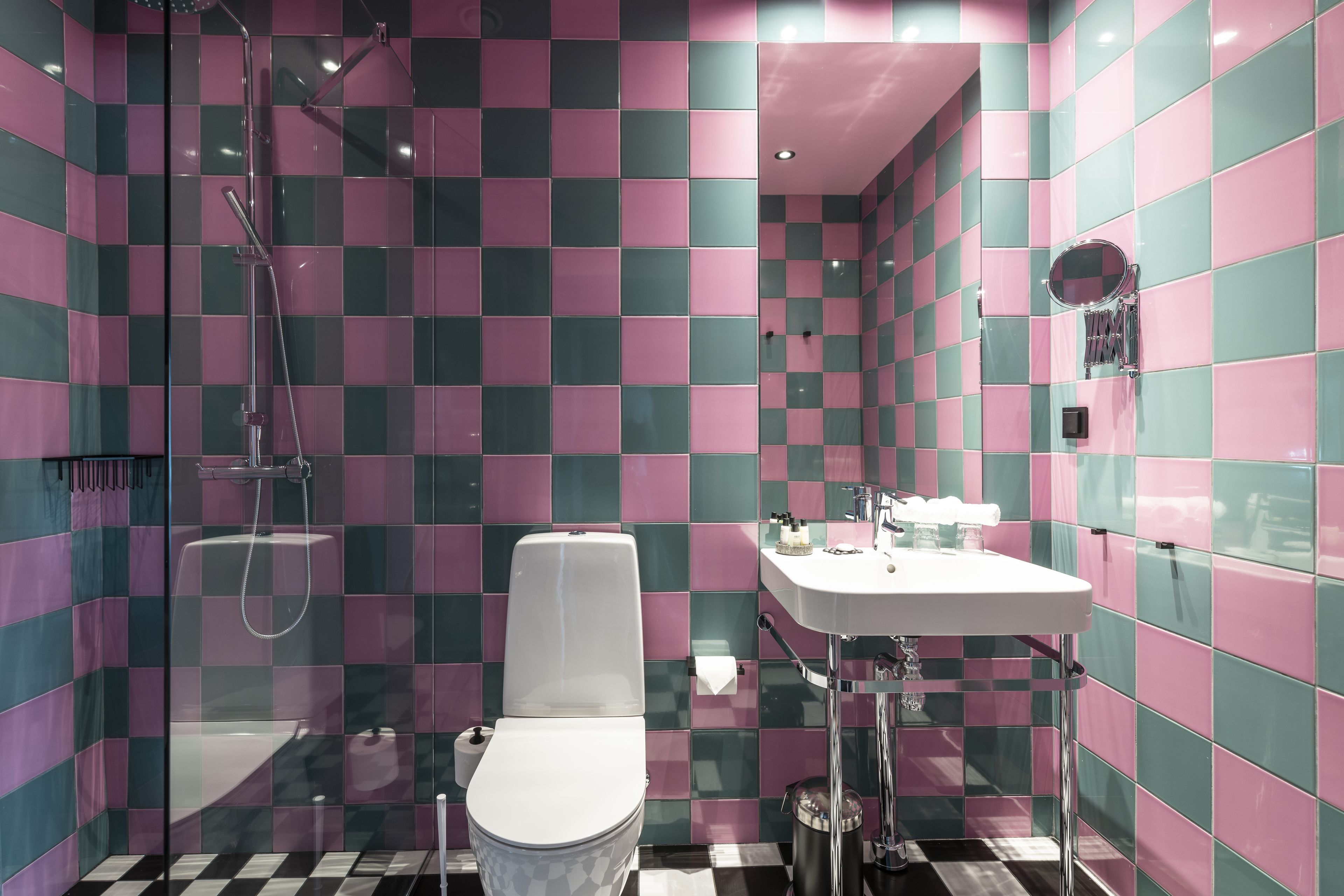 A bathroom with a checkered tile pattern, a toilet, a sink, and a shower.