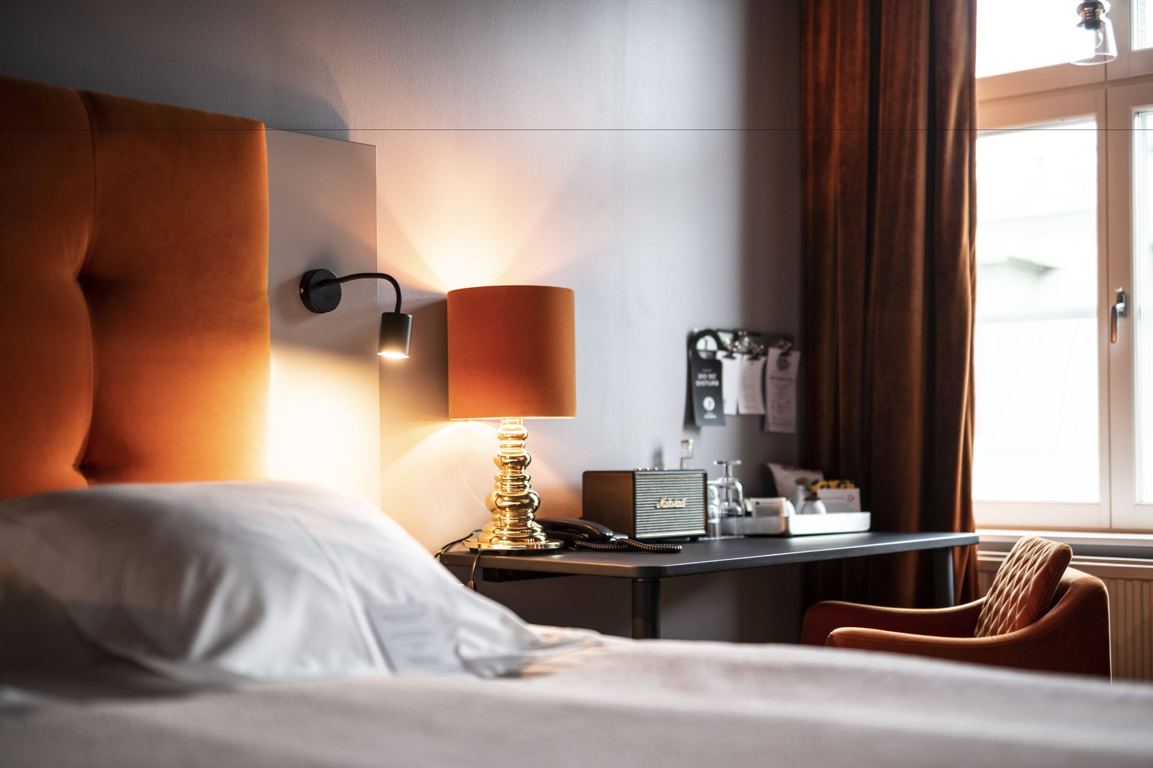 Une chambre d’hôtel avec un lit, un bureau doté d’une lampe, une chaise et une fenêtre avec des rideaux.