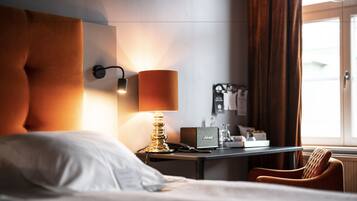 Une chambre d’hôtel avec un lit, un bureau doté d’une lampe, une chaise et une fenêtre avec des rideaux.