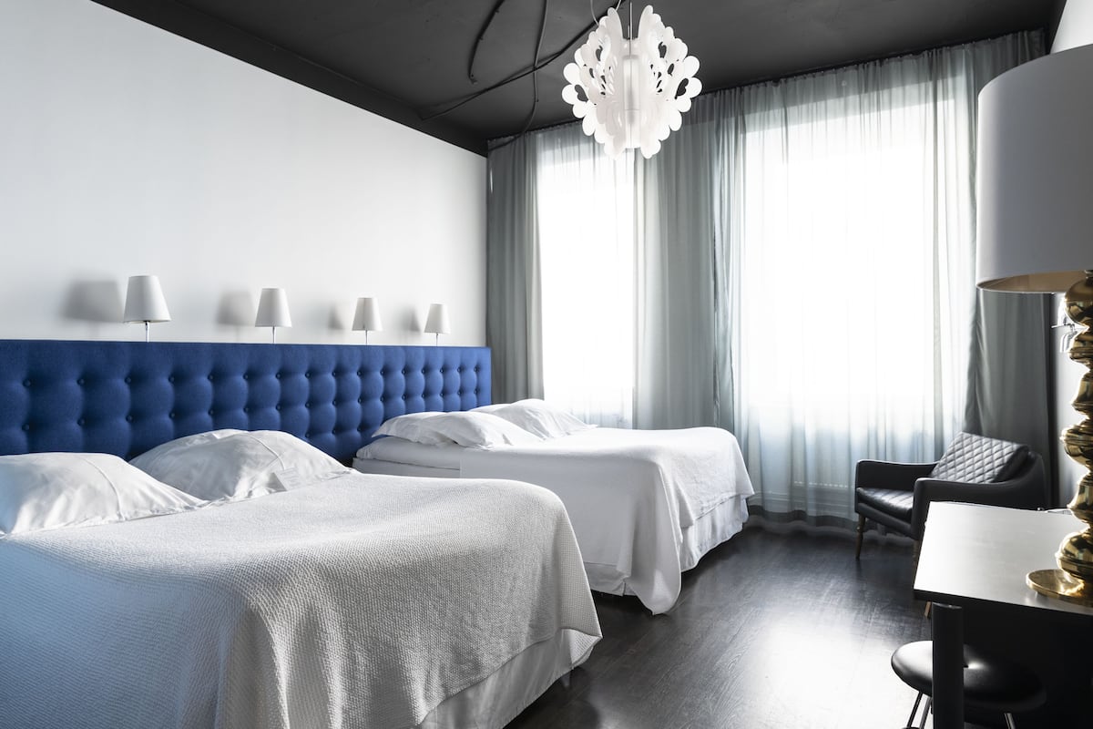 A hotel room with two beds, a blue headboard, a chandelier, a desk, and a chair.