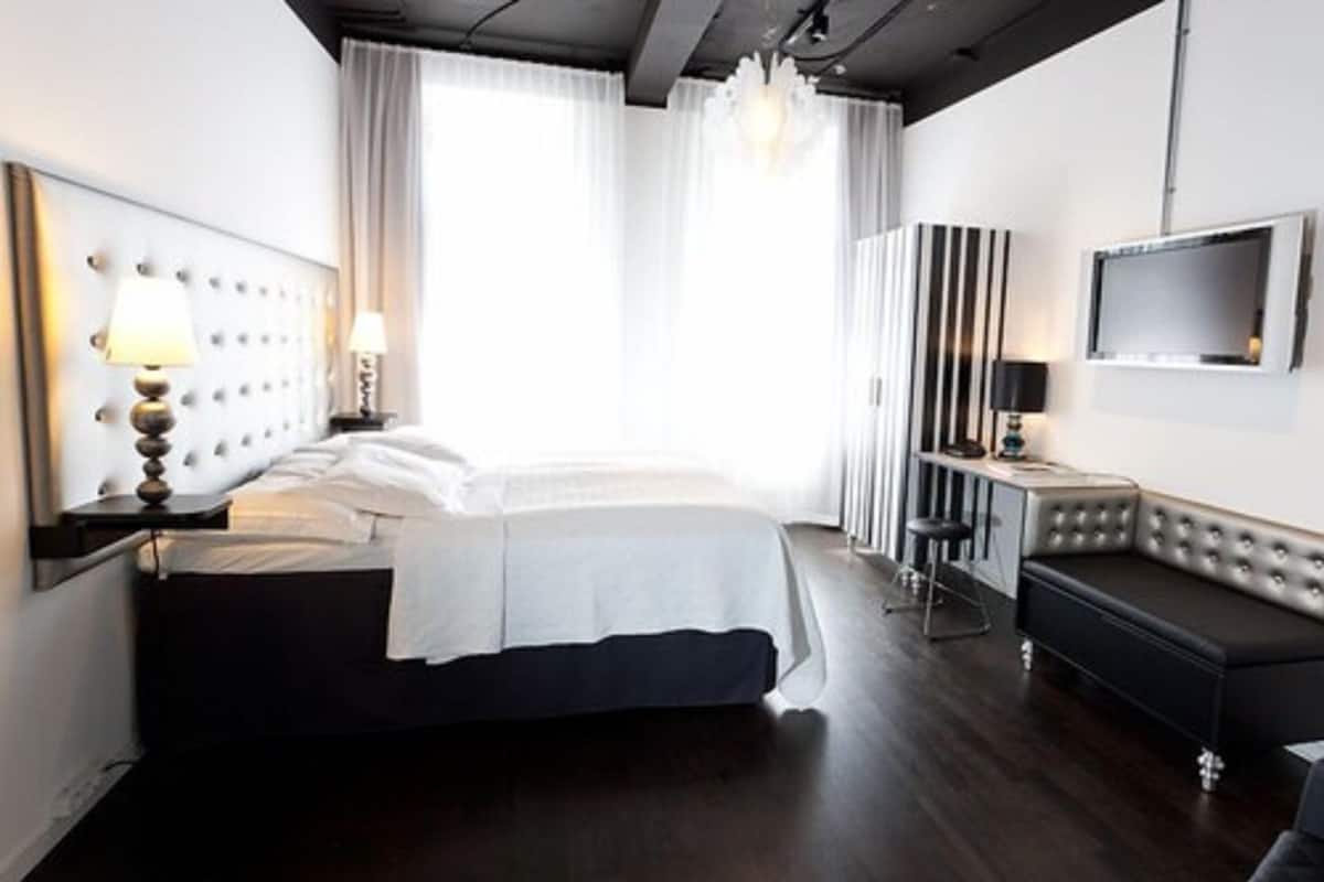 A modern hotel room with a large bed, a desk with a chair, a TV mounted on the wall, and a sofa.