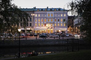 A hotel with a classic facade, a visible entrance, and a street view with parked cars and a canal. - Hotel Flora (Gothenburg)