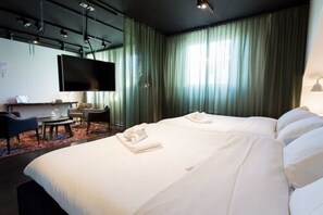 A hotel room with a large bed, a desk with a chair, a flat-screen TV, and a large window with curtains. - Hotel Flora (Gothenburg)