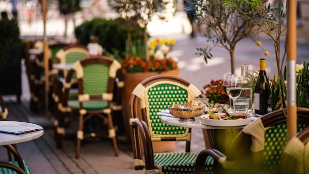An outdoor dining area with wicker chairs and tables, a variety of plants, and a bottle of wine on the table. - Hotel Flora (Gothenburg)