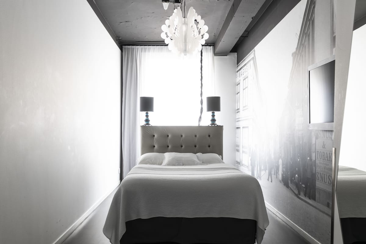A bedroom with a large bed, two bedside lamps, a chandelier, and a view of a street scene through a window.
