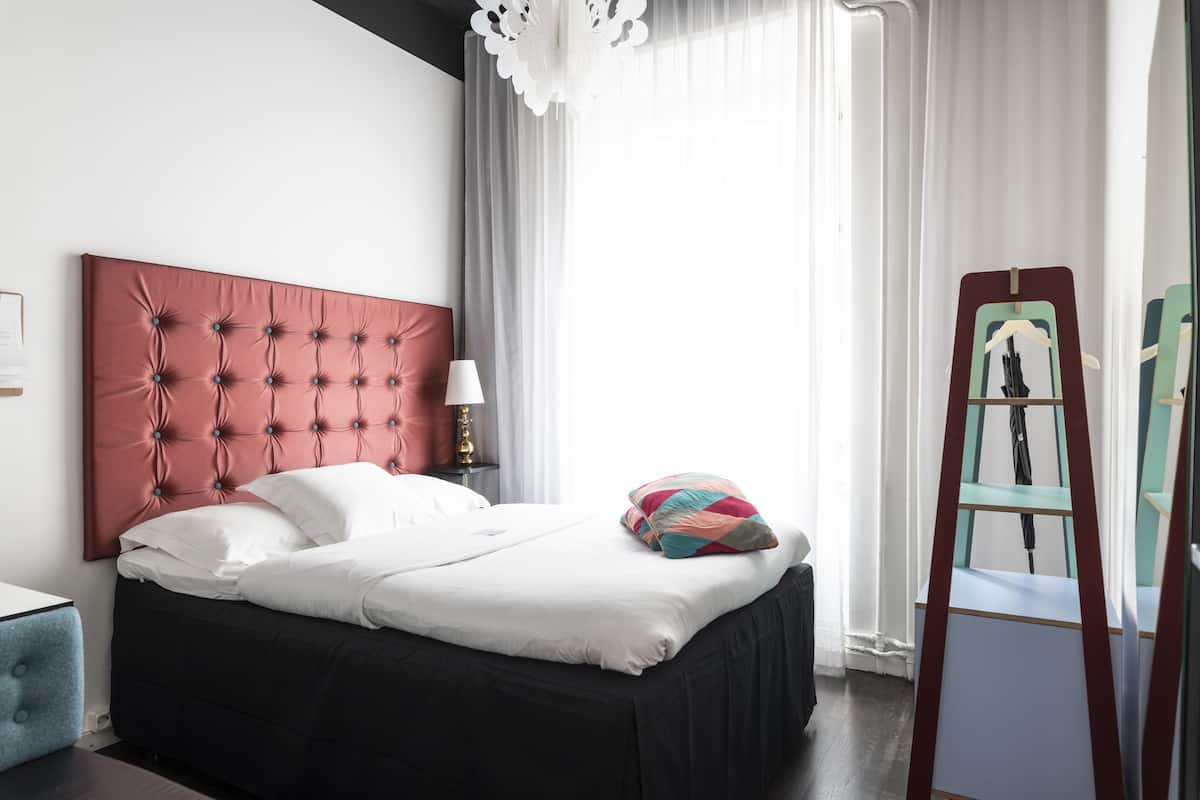 A neatly made bed with a red headboard, a bedside table with a lamp, and a ladder against the wall.