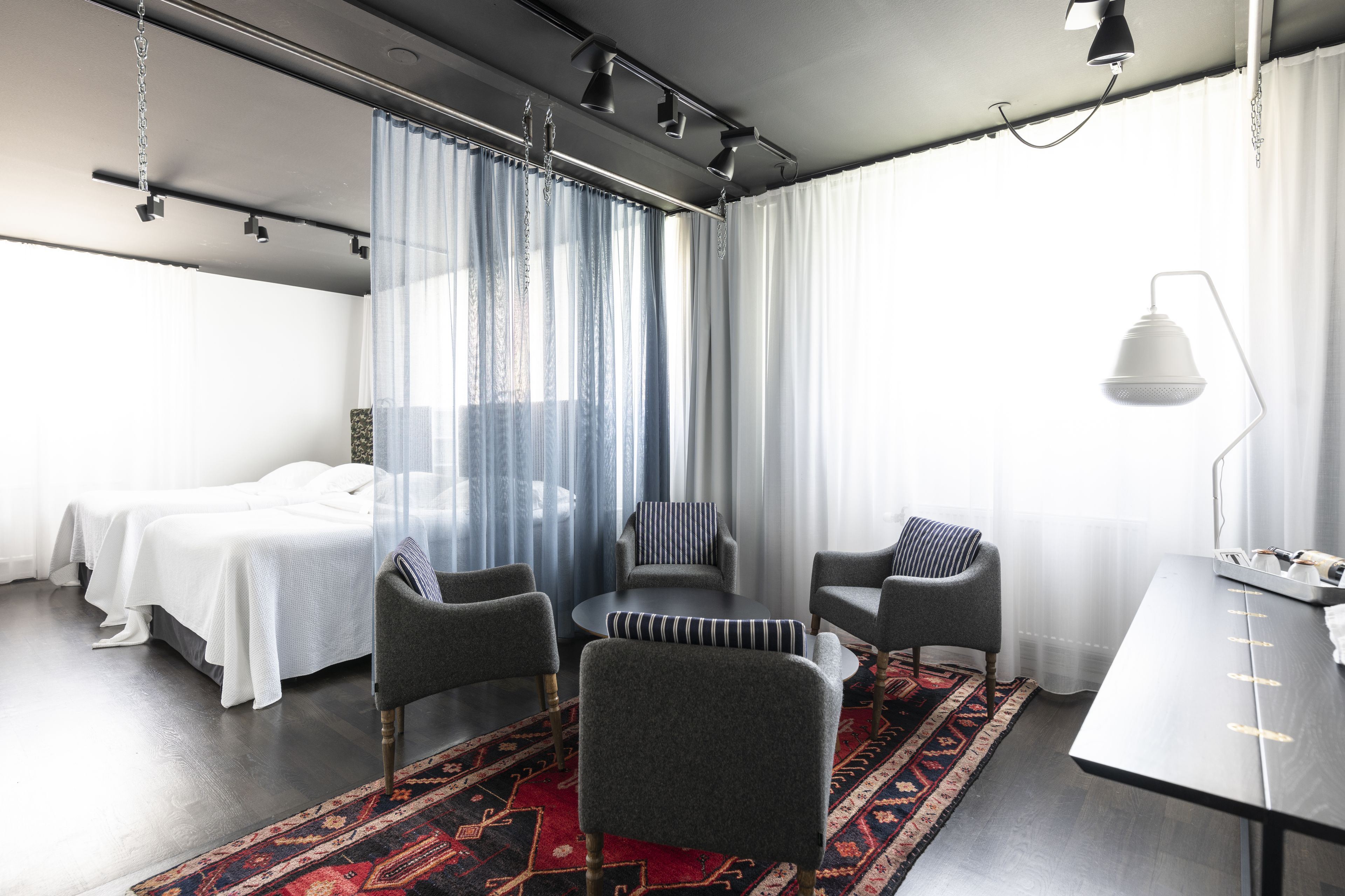 A hotel room with a bed, two armchairs, a small table, and a desk.