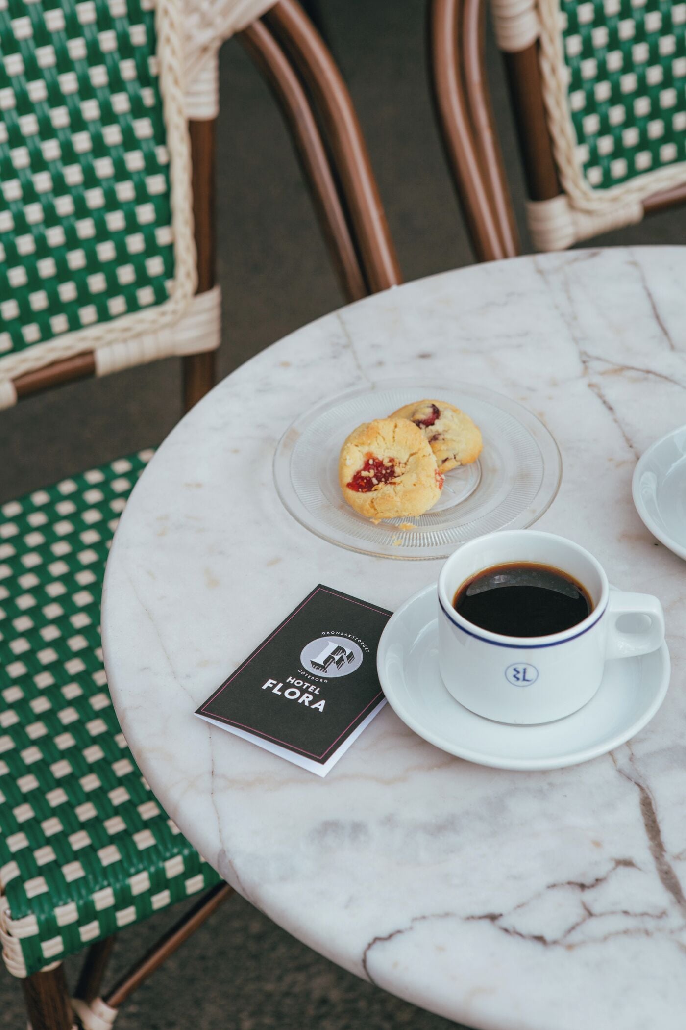 Een ronde marmeren tafel met een glazen plaat waarop een muffin, een kop koffie en een menukaart staan.