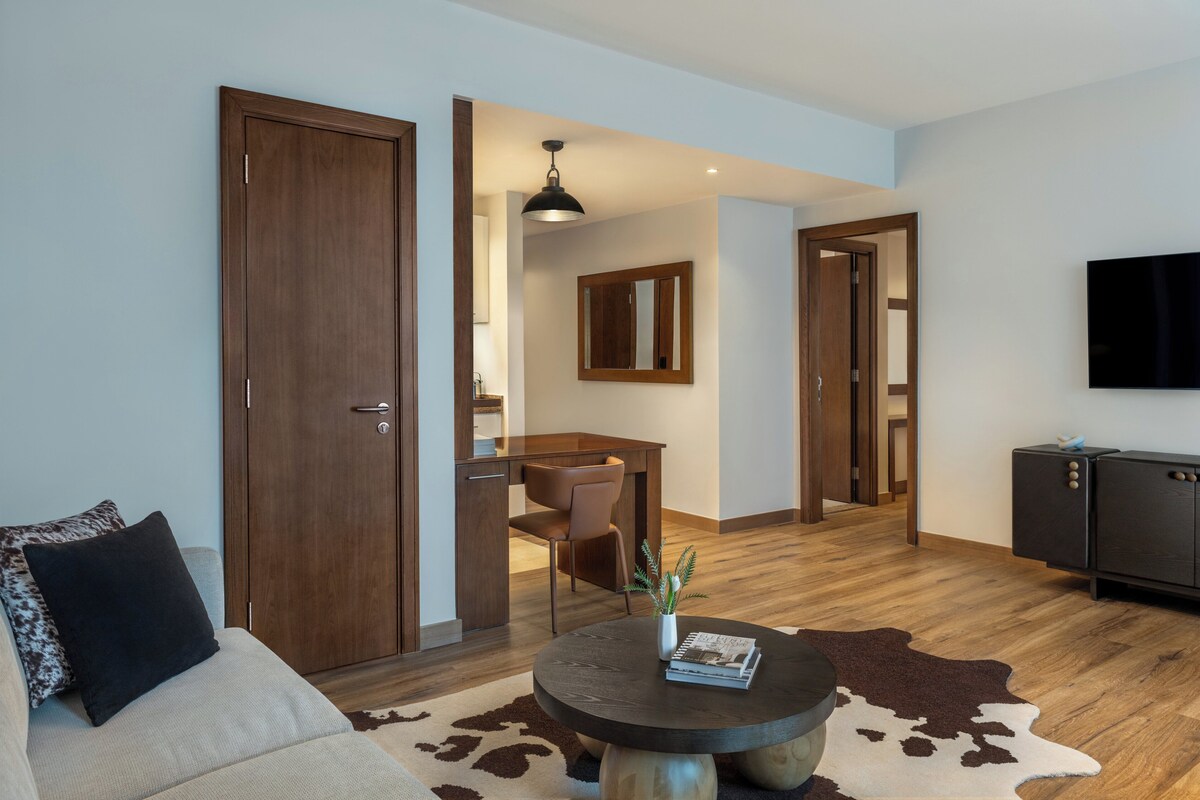 Una sala de estar moderna con un sofá, una mesa de centro redonda, un tapete de cuero de vaca, una mesa de comedor de madera y un televisor montado en la pared.