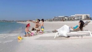 Eine Strandansicht mit blauem Himmel, sandigem Ufer und einigen Personen.