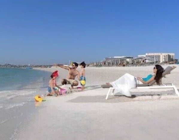 A beach scene with a clear sky, a sandy shore, and a few people.