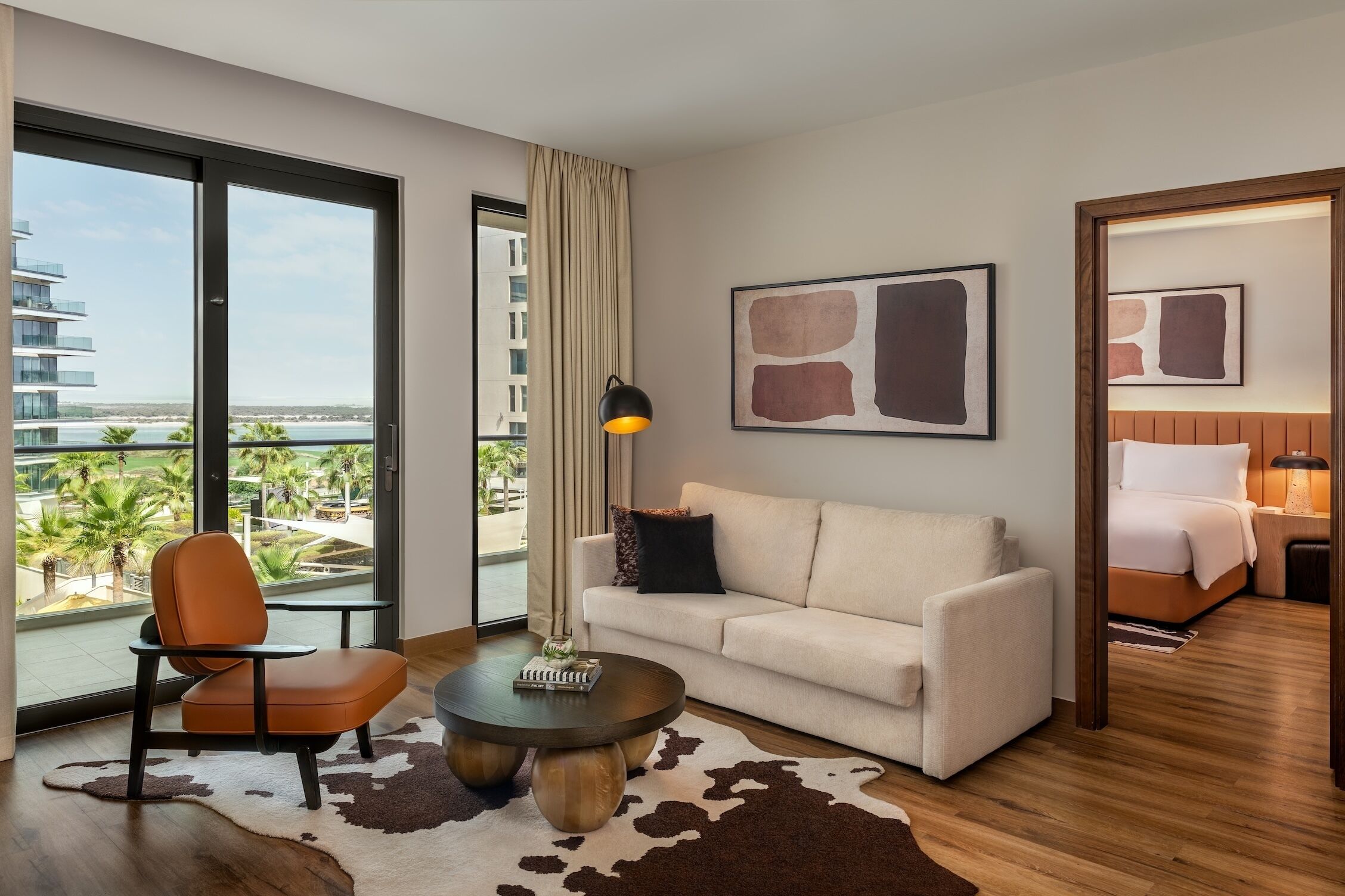 A modern hotel room with a large window, a sofa, a coffee table, and a view of the beach.