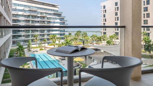 Ein Balkon mit Blick auf einen Swimmingpool, Palmen und moderne Gebäude.