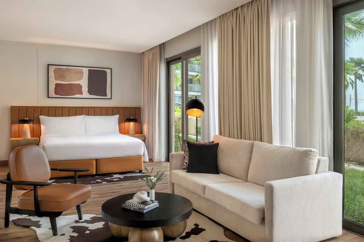 Ein Hotelzimmer mit Bett, einer Couch, einem Sessel, einem Couchtisch und einem großen Fenster mit Vorhängen.