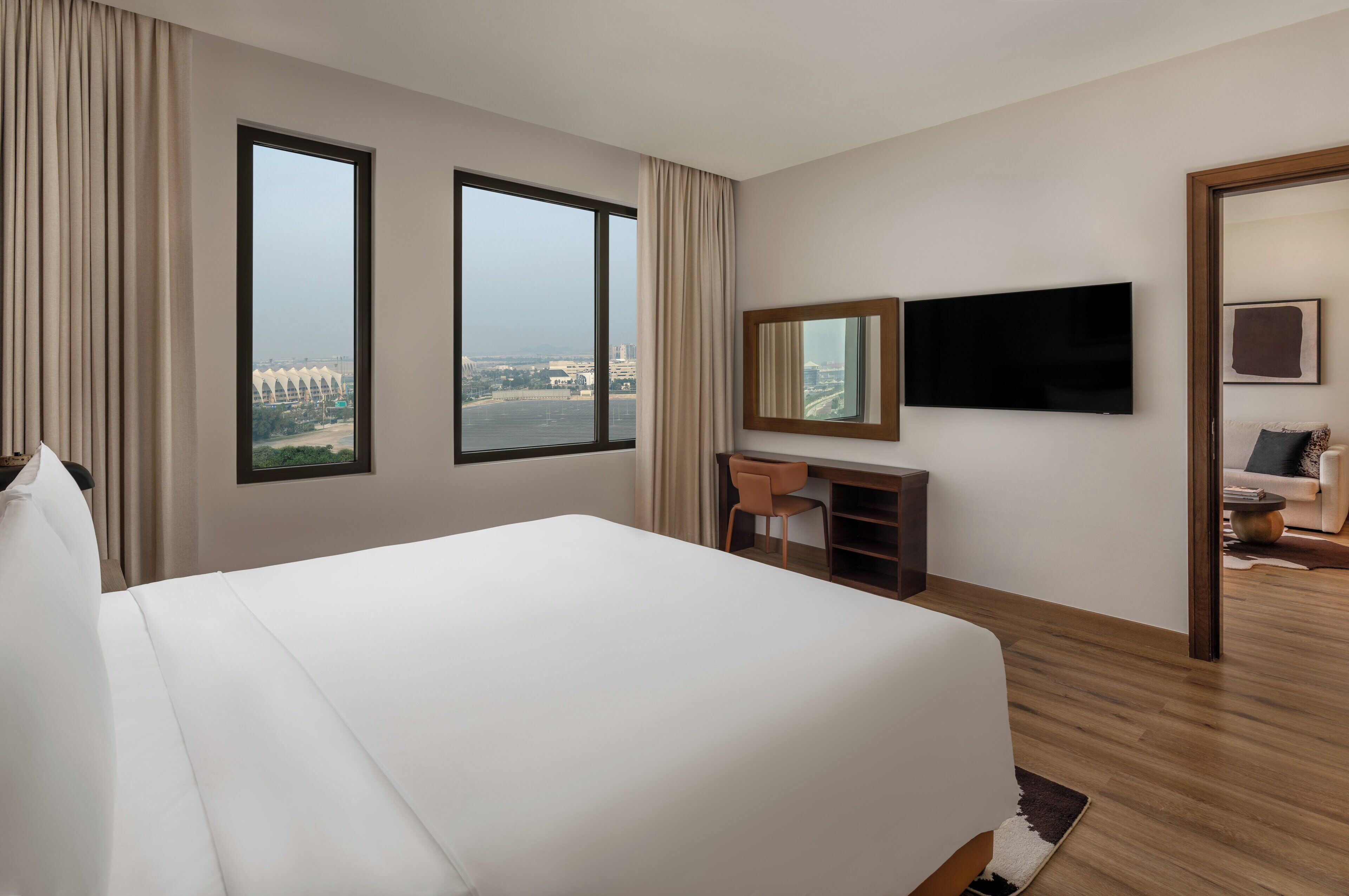 A hotel room with a large bed, a desk, a chair, a TV, and a view of a cityscape.