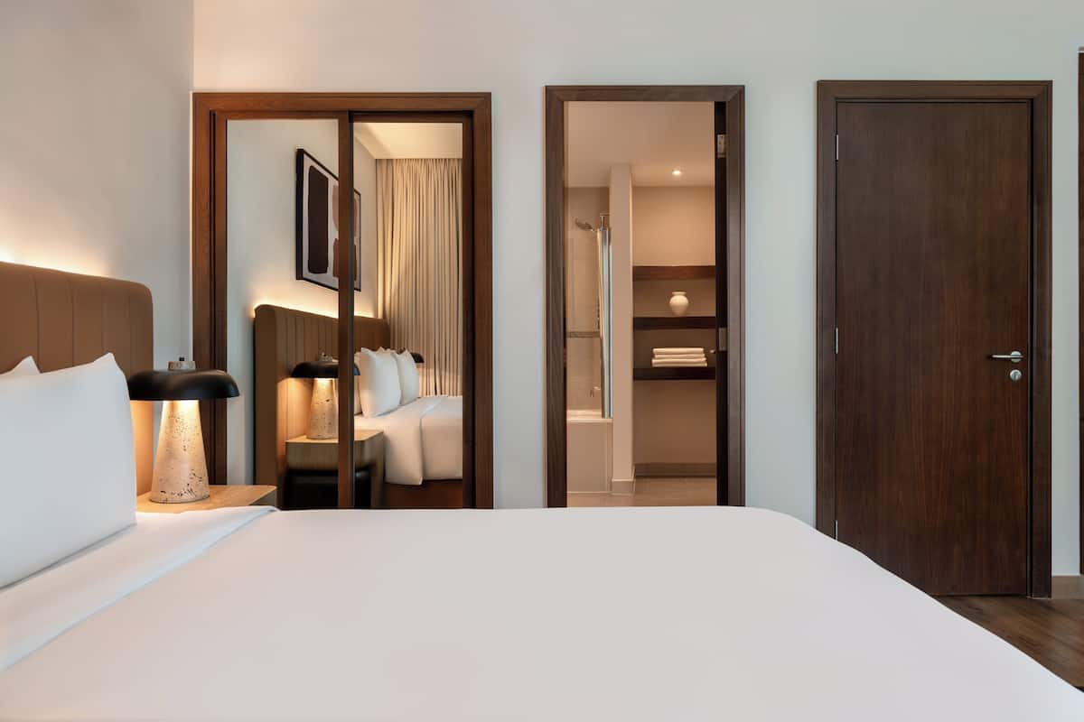 Ein Hotelzimmer mit Bett, Nachttischlampe, Spiegel, Tür und Duschbereich.
