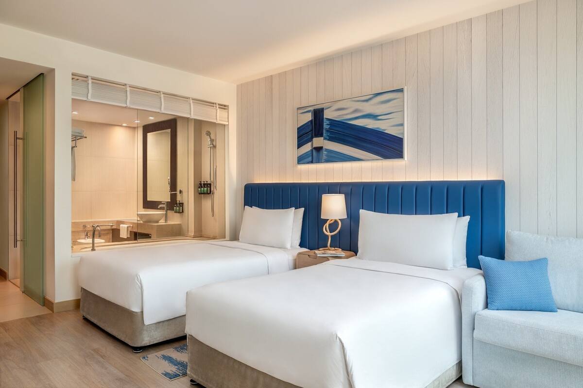 A hotel room with two beds, a large mirror, a bathroom with a sink, and a blue accent wall.
