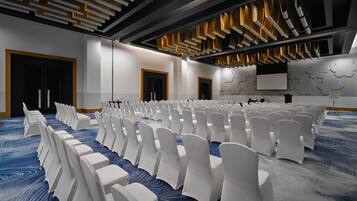 A conference room with rows of white chairs, a patterned carpet, and a modern ceiling design.