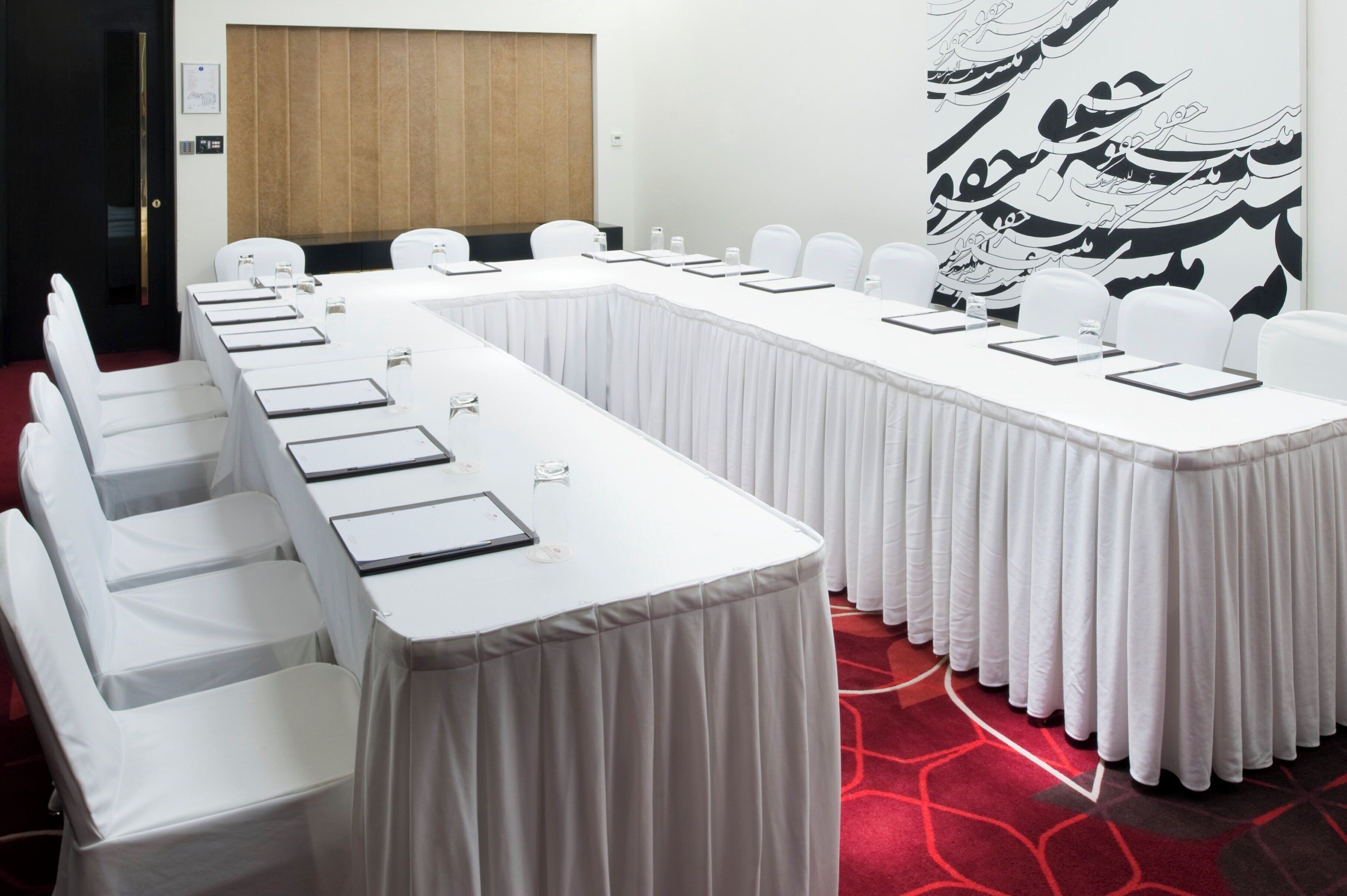 A conference room with long tables, white chairs, and a red carpeted floor.