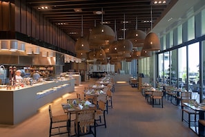 Enjoy dining in a spacious restaurant with a central bar area and rows of dining tables and chairs.