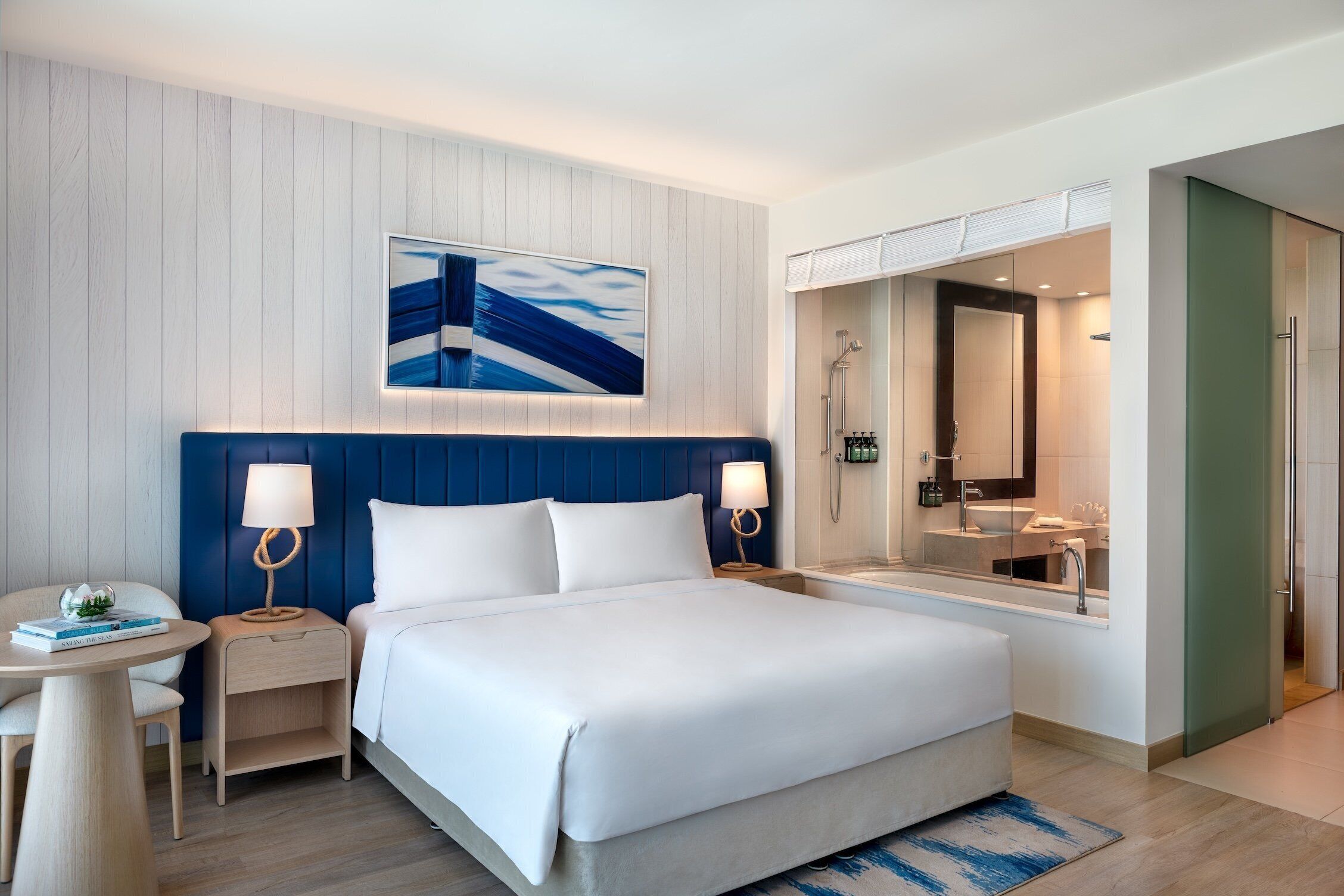 Una camera d'albergo moderna con un letto grande, comodini, una scrivania e un bagno con uno specchio e un lavandino.