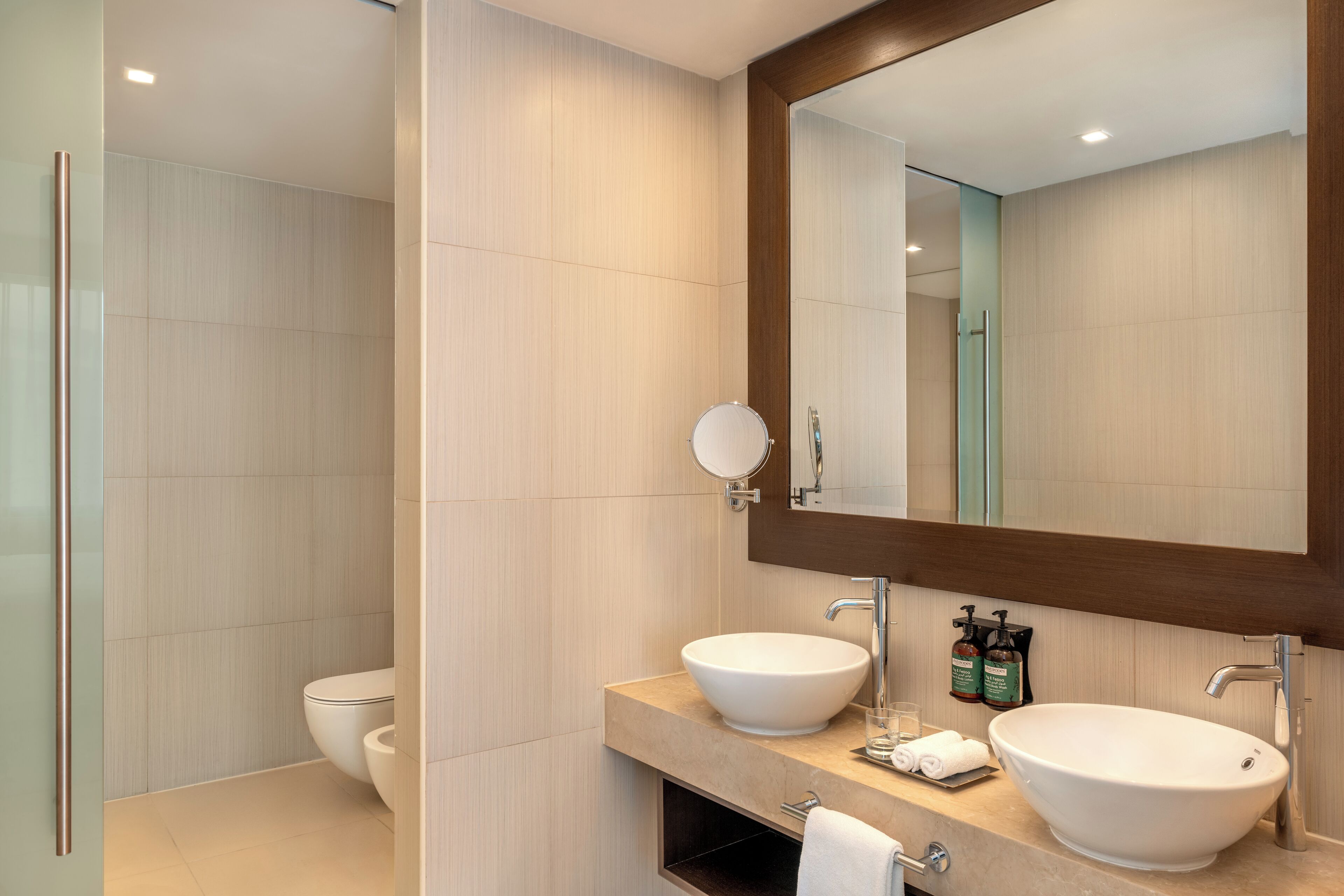 A modern bathroom with two sinks, a large mirror, and a toilet.