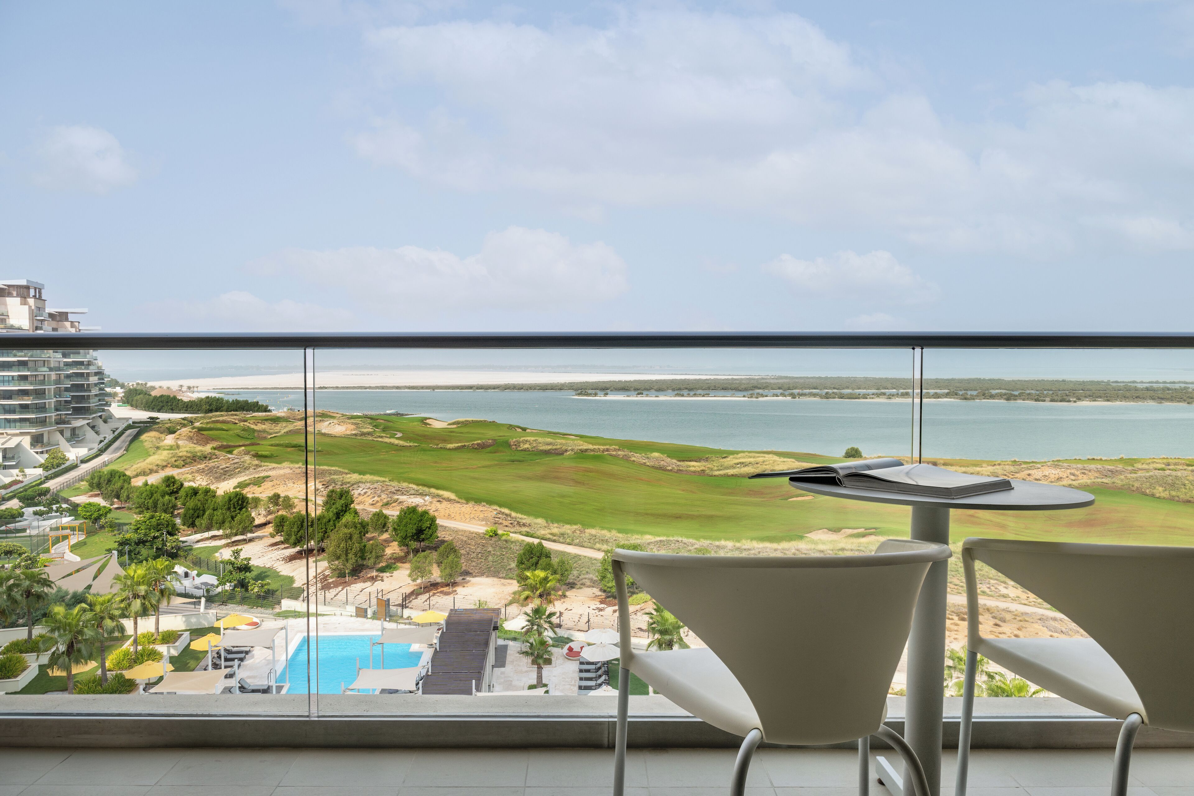 A balcony with a view of a golf course, a pool, and a beach.