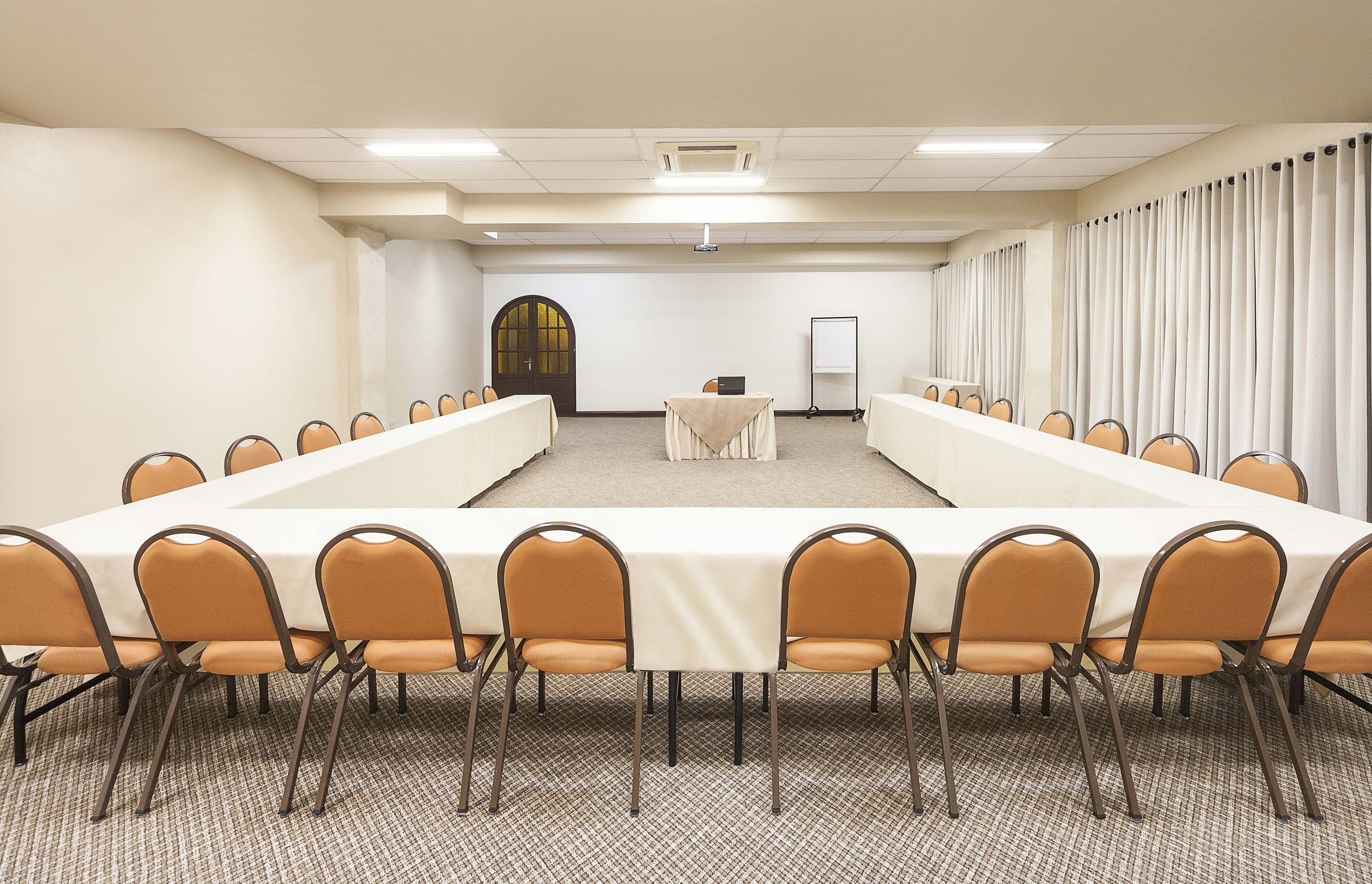 Un salón de conferencias con una larga mesa, sillas, un proyector y una pizarra.