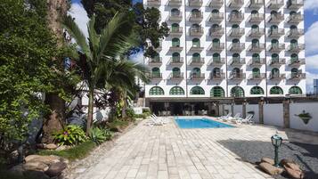 Un hotel con zona de piscina, mobiliario exterior y un edificio grande con varios balcones.