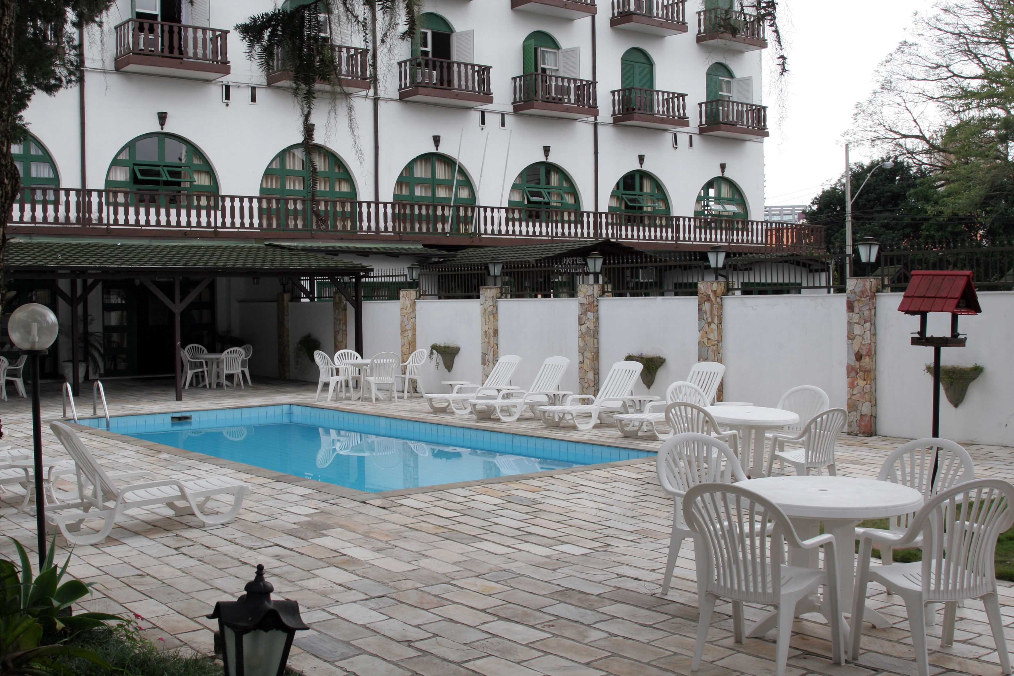 A pool area with lounge chairs and tables, a white building with balconies, and a stone wall.
