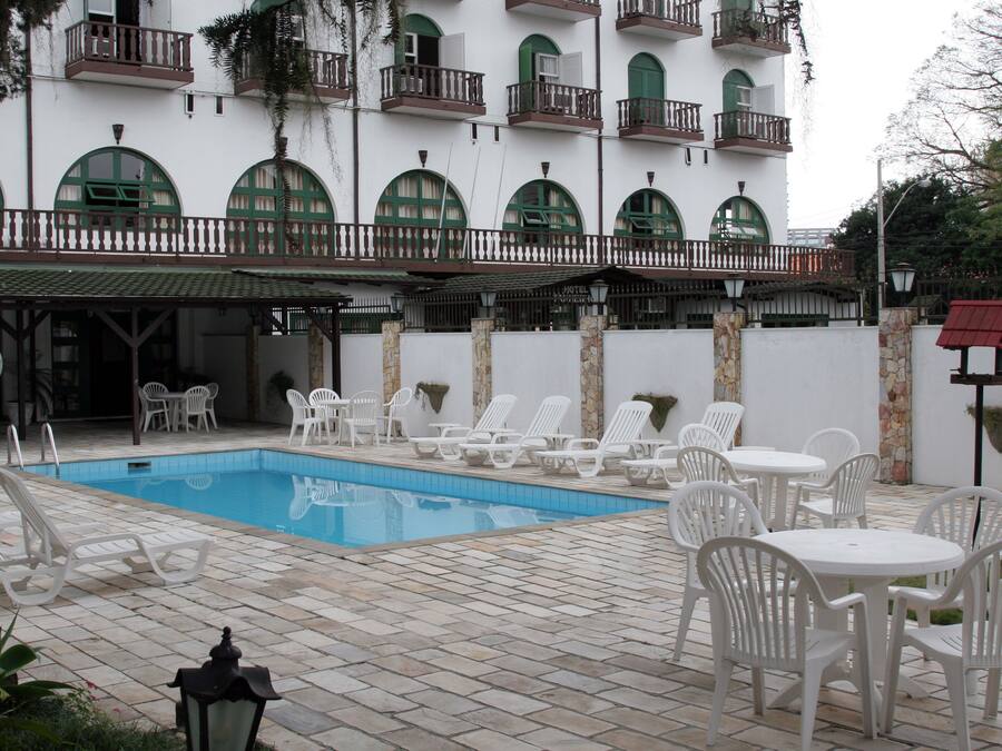 A pool area with lounge chairs and tables, a white building with balconies, and a stone wall.