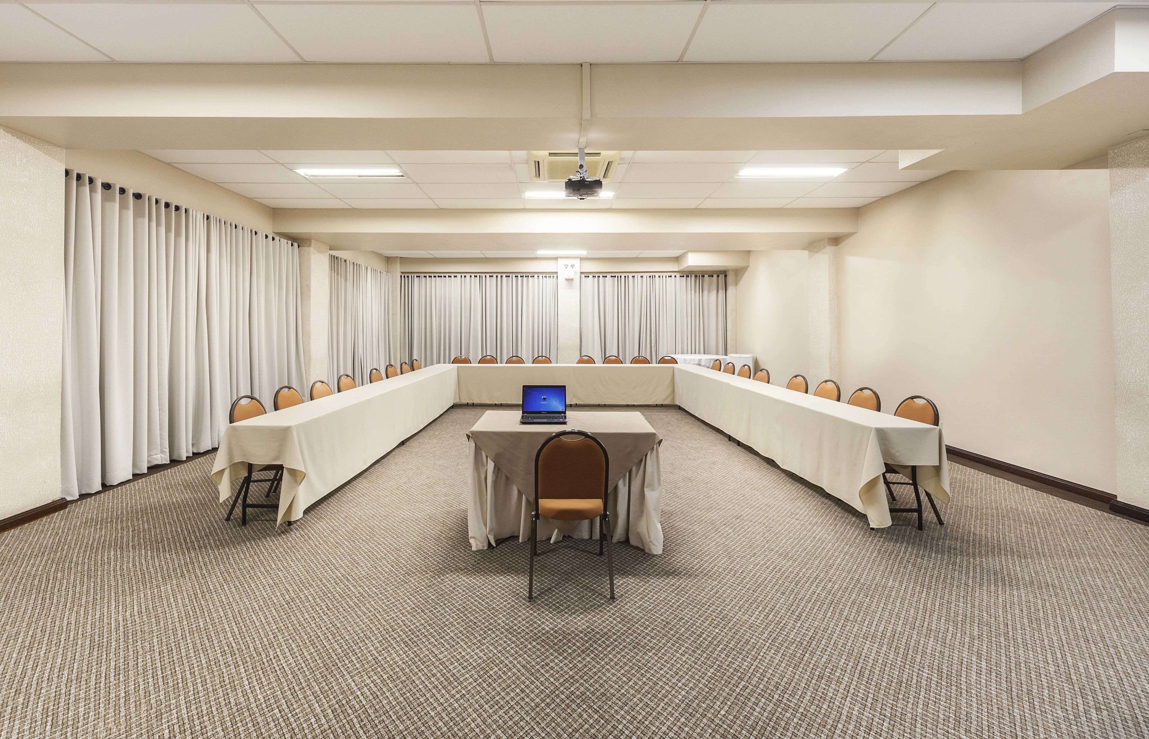 Un salón de conferencias con una larga mesa, sillas, una computadora portátil y un proyector.