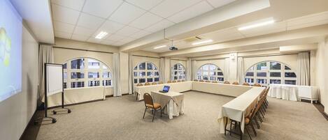 A conference room with a long table, chairs, a laptop, and a projector screen.