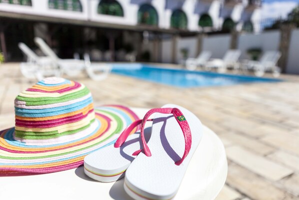 A pair of white flip-flops with pink straps and a colorful striped hat on a white surface.