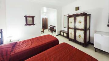 A room with two beds, a wooden cabinet, a small table with chairs, and a white refrigerator.