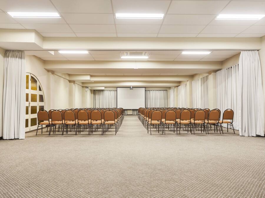 A conference room with rows of chairs, a projector screen, and curtains.