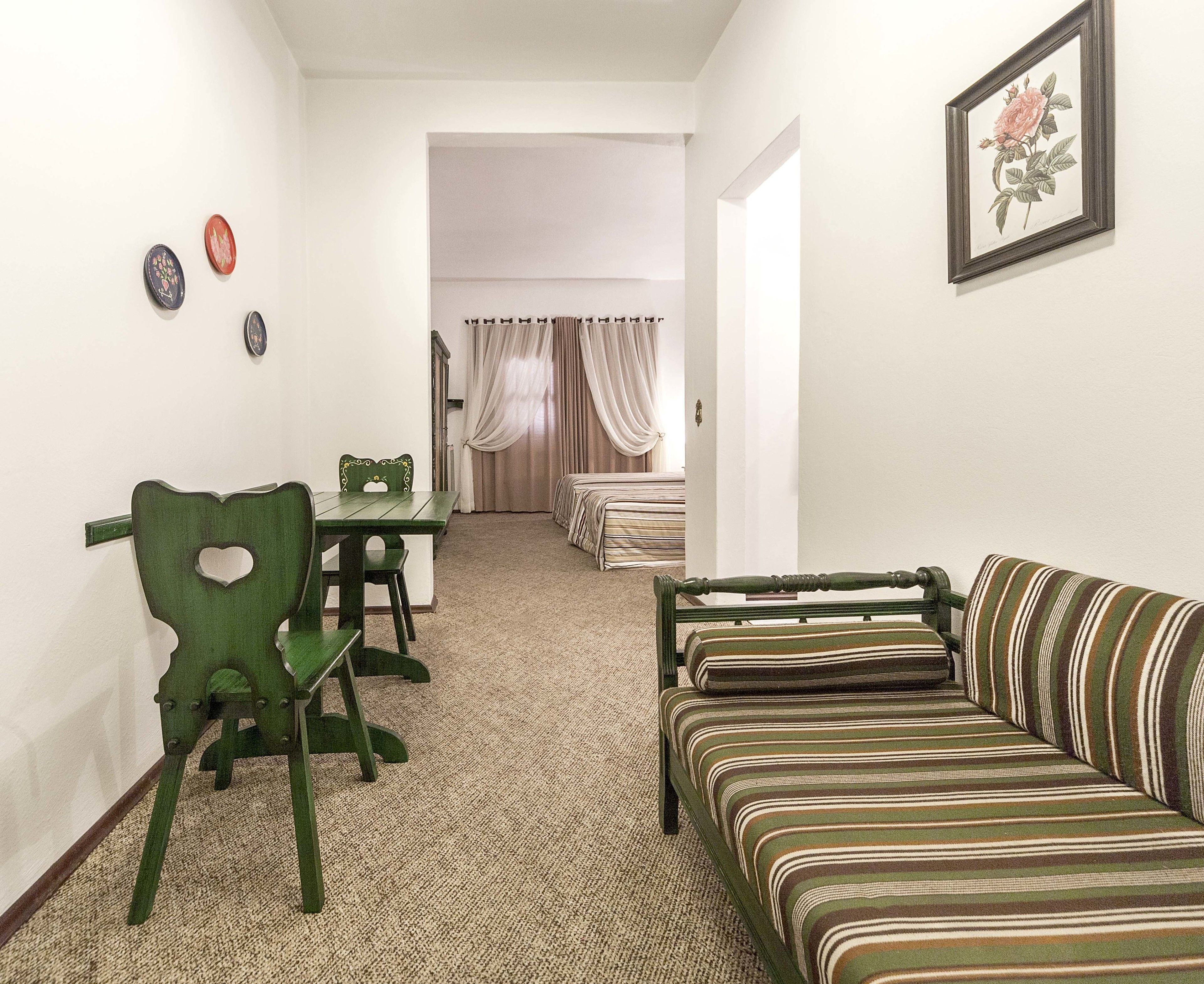A room with a striped sofa, a green chair with a heart cutout, a dining table, and a bed with striped bedding.