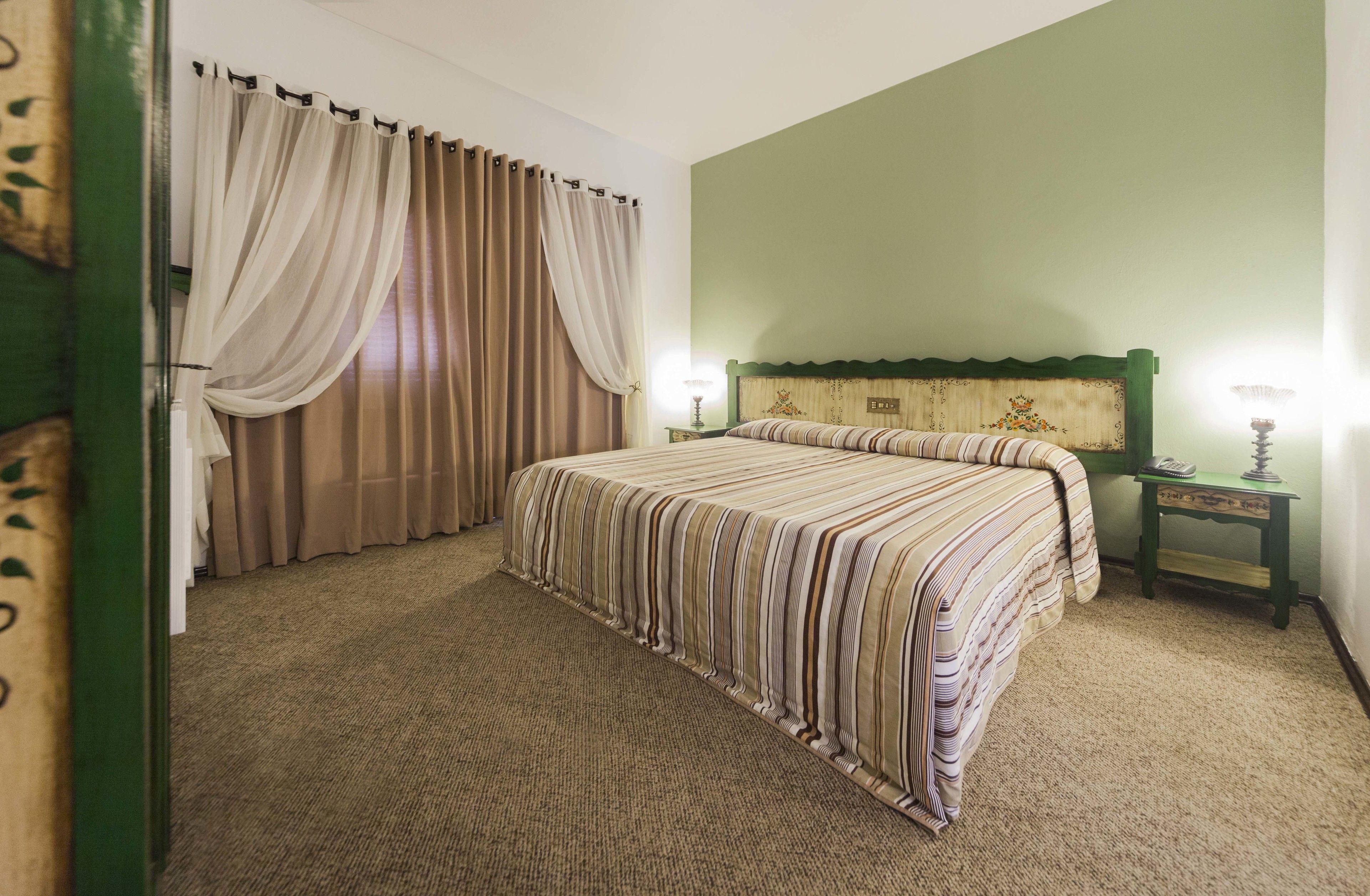 A hotel room with a bed, curtains, a nightstand, and a lamp.