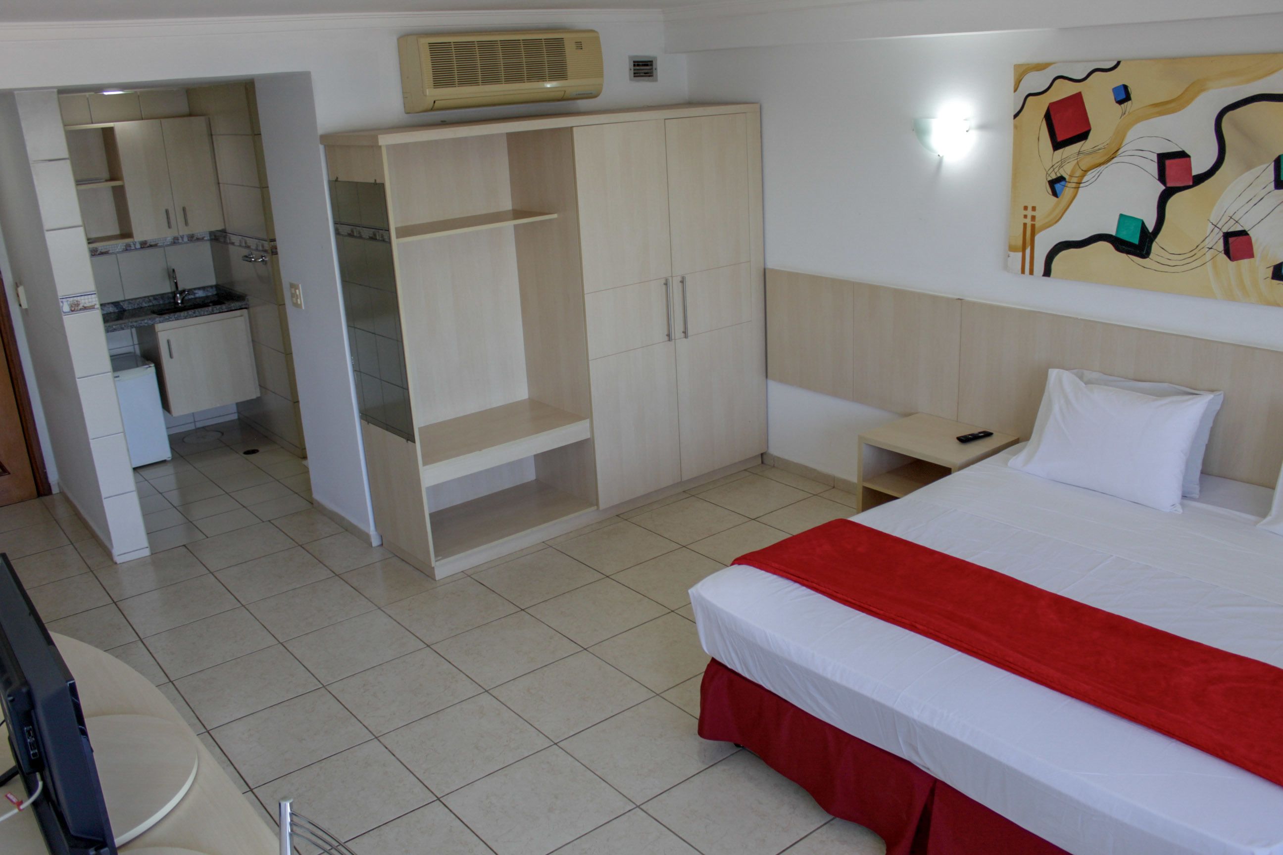 A hotel room with a bed, a TV, a kitchenette, and a wardrobe.