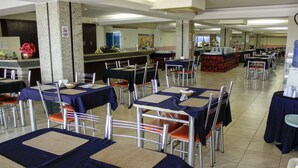 Een ruime eetruimte met meerdere tafels en stoelen, een buffetopstelling en een counter met een bloemstuk.