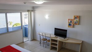 Een hotelkamer met een bed, een bureau met een computerscherm, een stoel en een raam met uitzicht op zee.