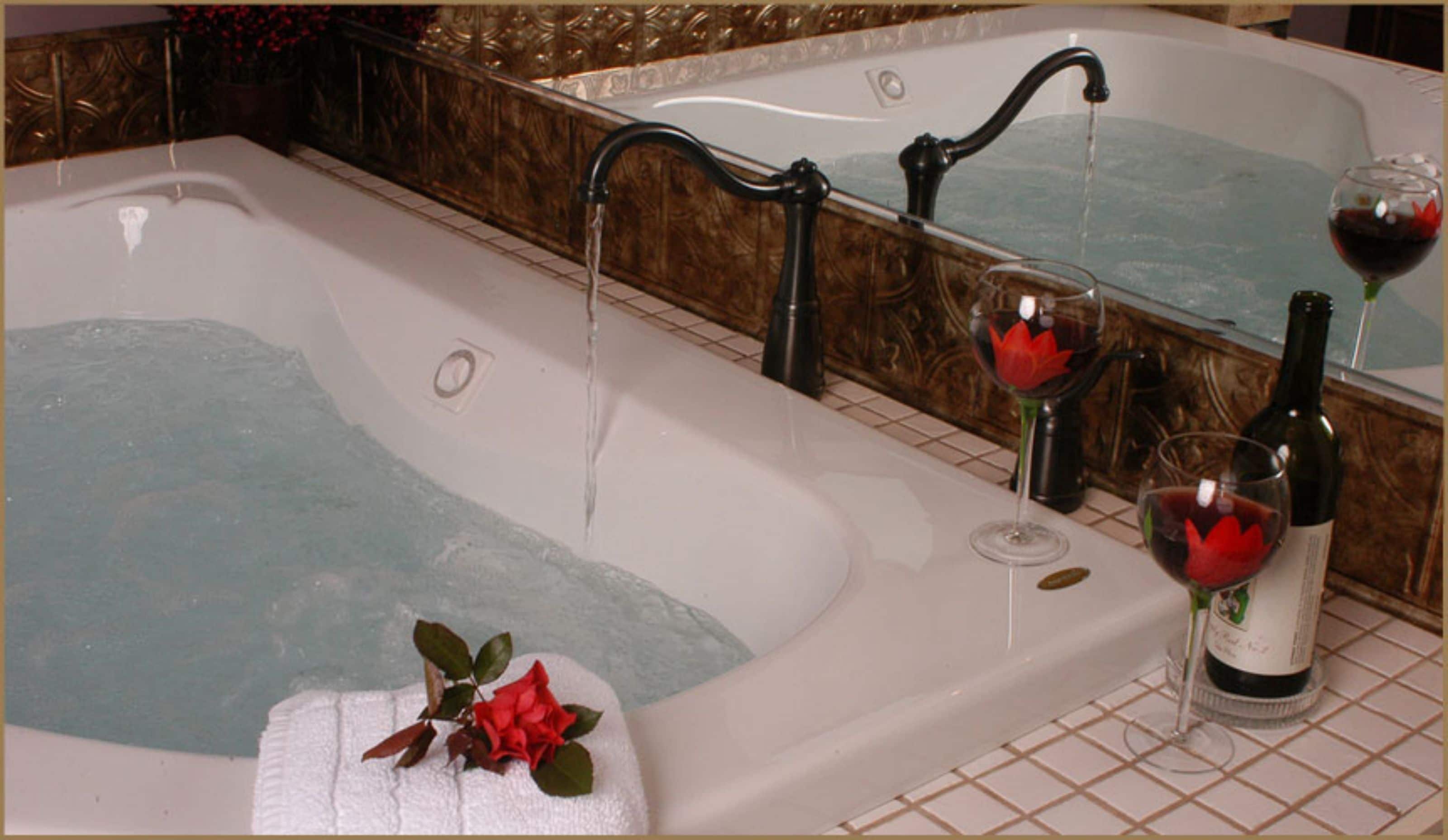 A bathtub with a faucet, two wine glasses with red flowers, and a wine bottle.